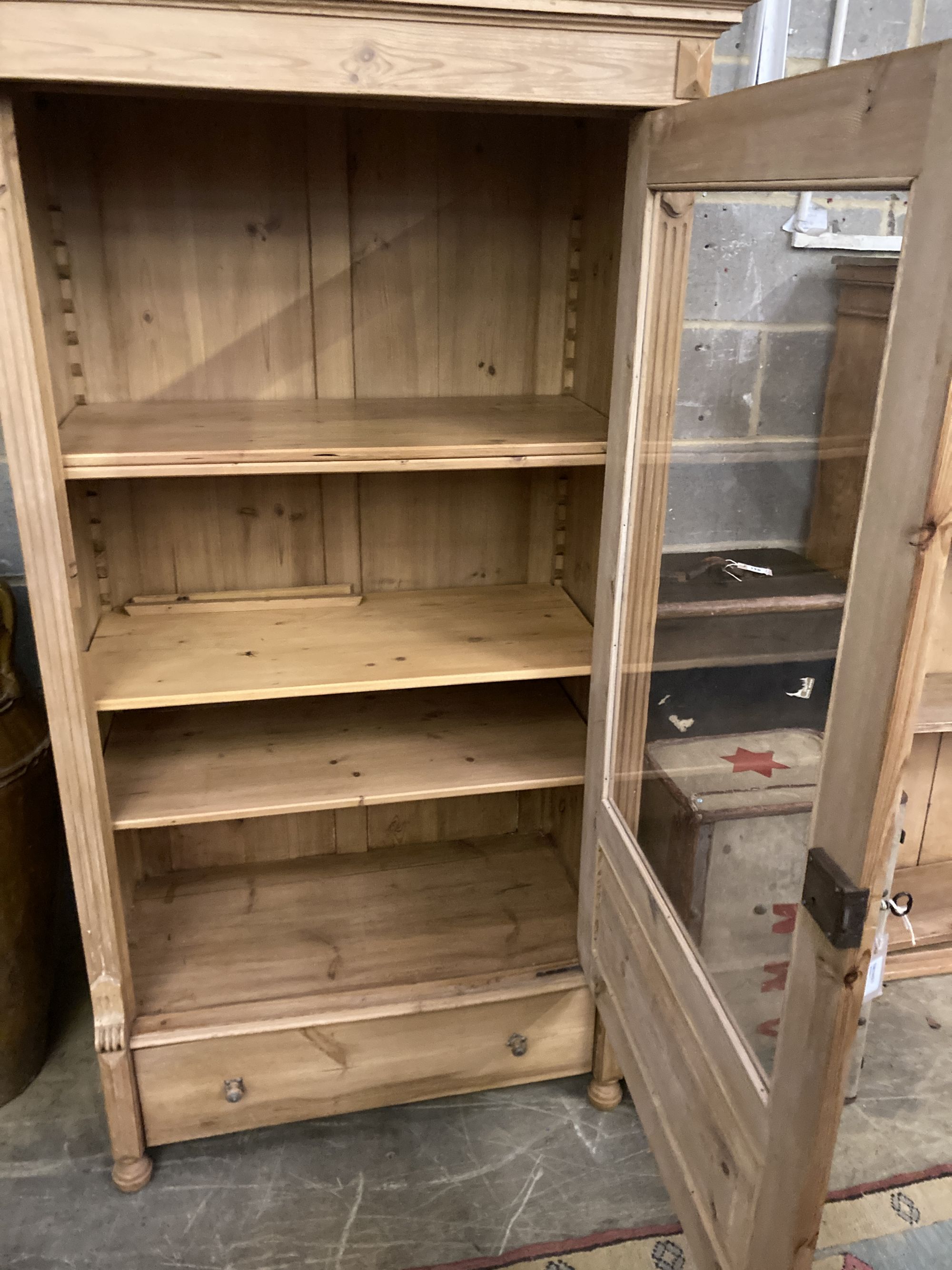 A pine display cabinet, fitted single glazed door enclosing four shelves over base drawer, width 100cm, depth 55cm, height 183cm